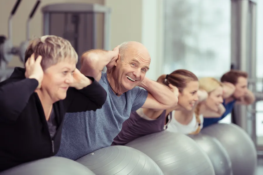 Mehrere Menschen unterschiedlichstem Alters, die Übungen mit einem Gymnastikball machen.