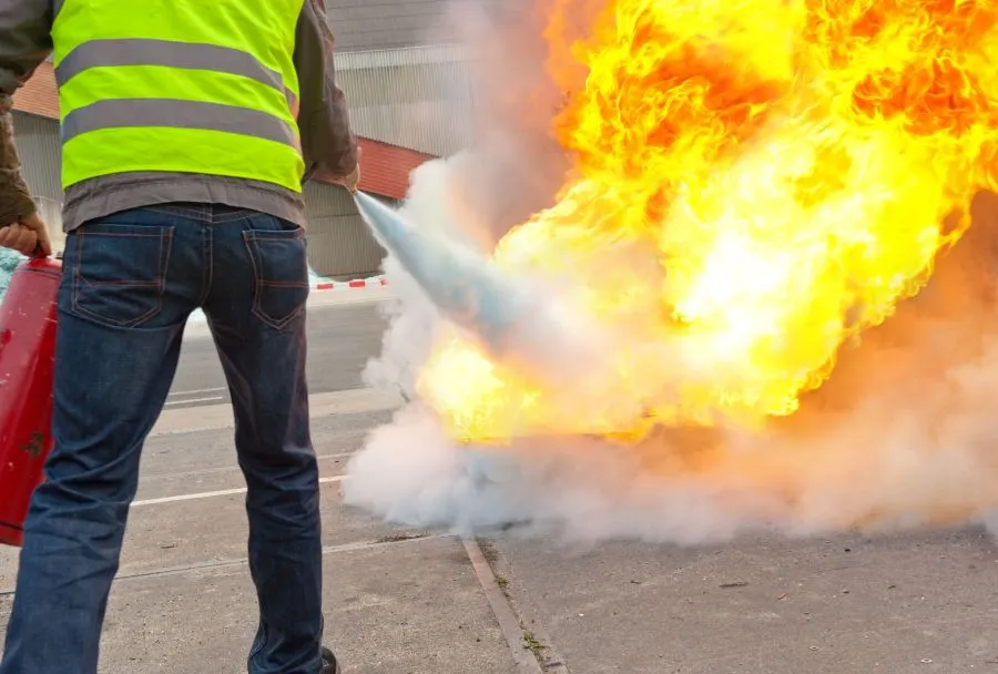 Person bedient Feuerlöscher um ein Feuer draußen zu löschen.