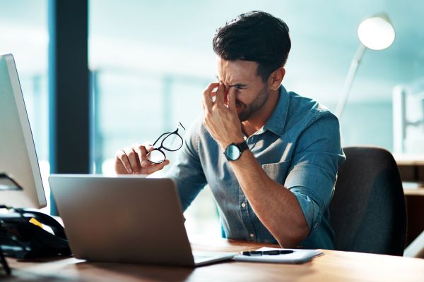 Mann am Schreibtisch reibt sich frustriert die Augen